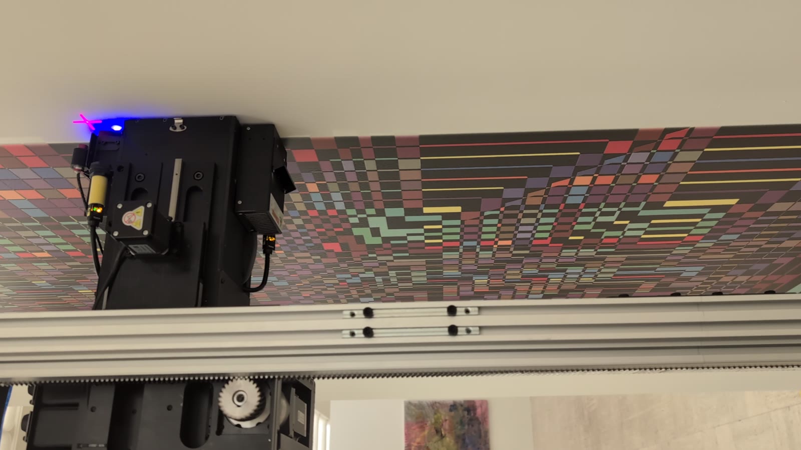 Close view of a vertical UV print head laying a color graphic onto a wall, a still from Bear Creek Murals’ site video.